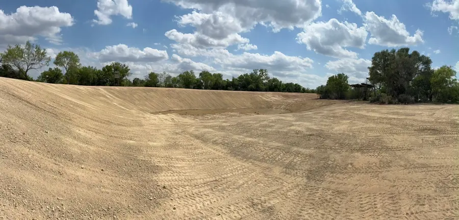 Wide graded earthwork basin with smooth sand-colored banks under a big cloudy sky
