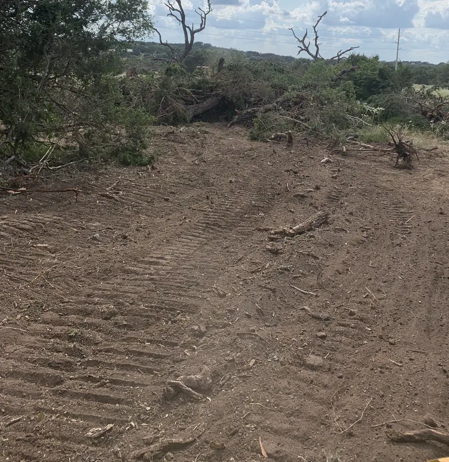 Fresh clearing seen from a machine cab, with track marks, pushed brush and dead trees along the edge