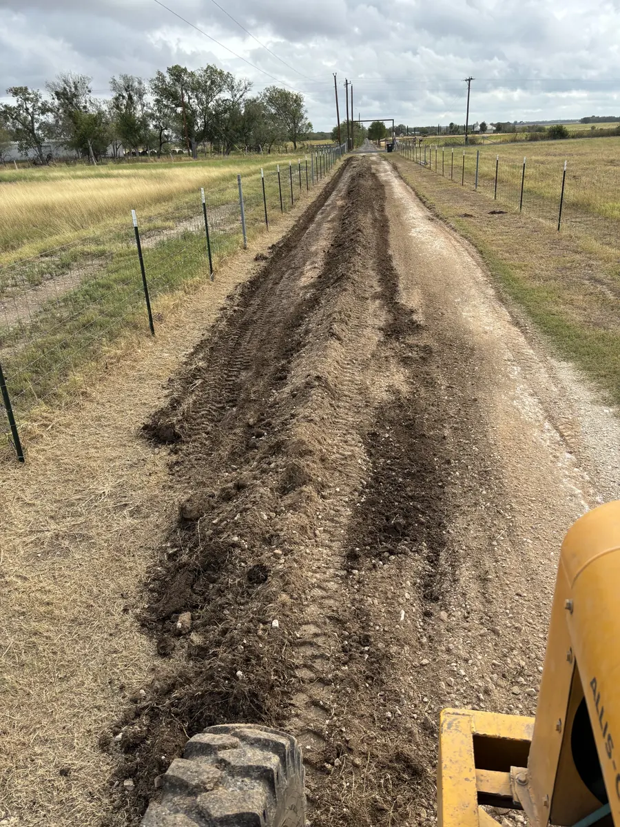 Freshly cut ditch running beside a fence line, with the grader's tire and blade in the corner