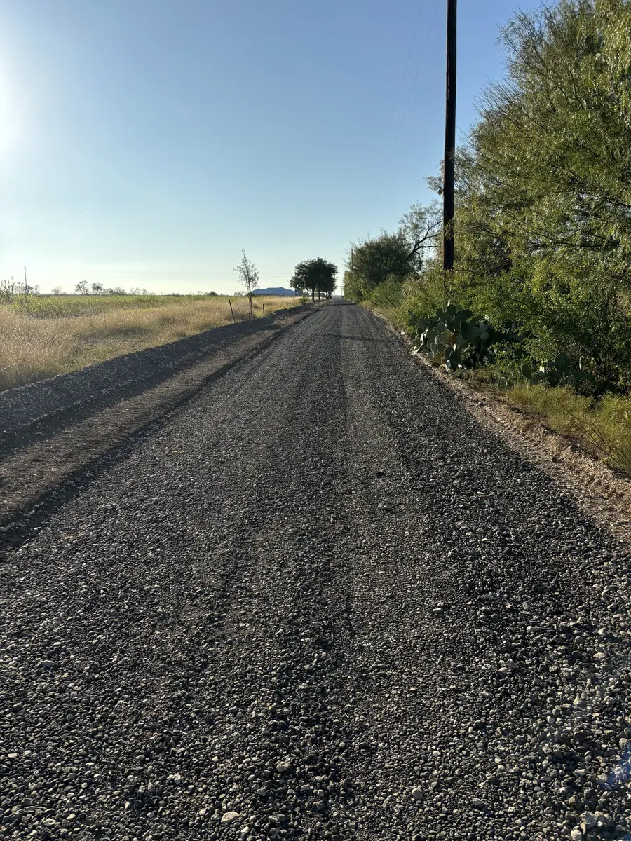 Straight drive with a dark crushed surface beside a tree line