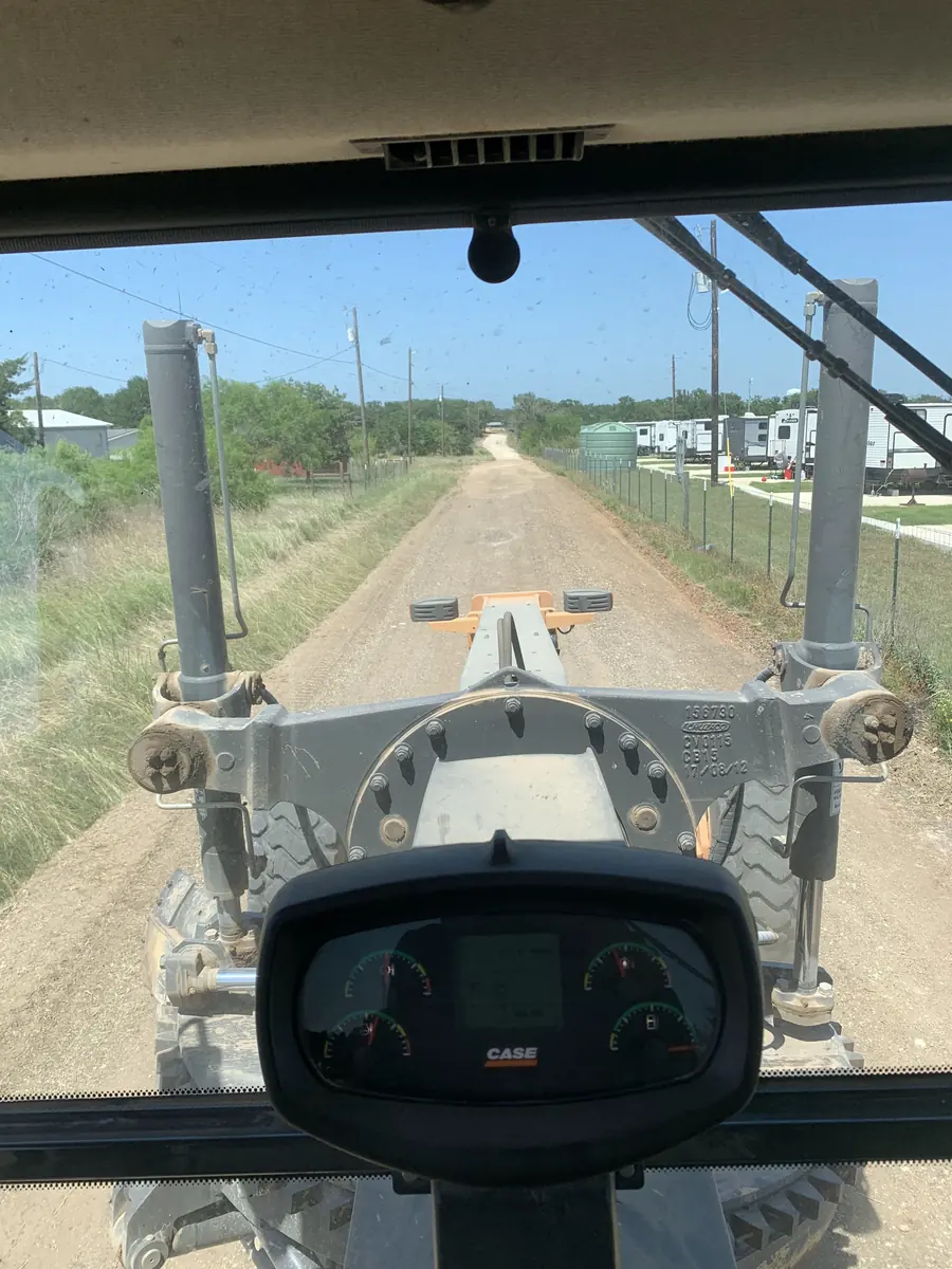 View from a motor grader cab down a long graded road between fences