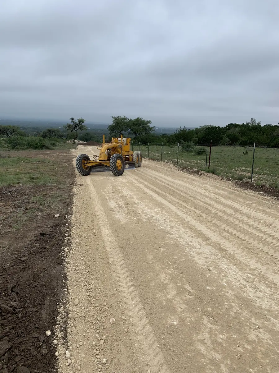 Motor grader working a wide graded road beside a fence line