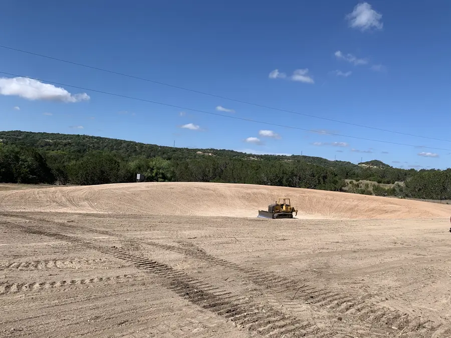 Dozer grading a wide open area on a hilltop, with wooded hills behind