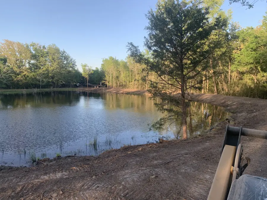 Pond full of water below tall trees, with part of a machine at the corner
