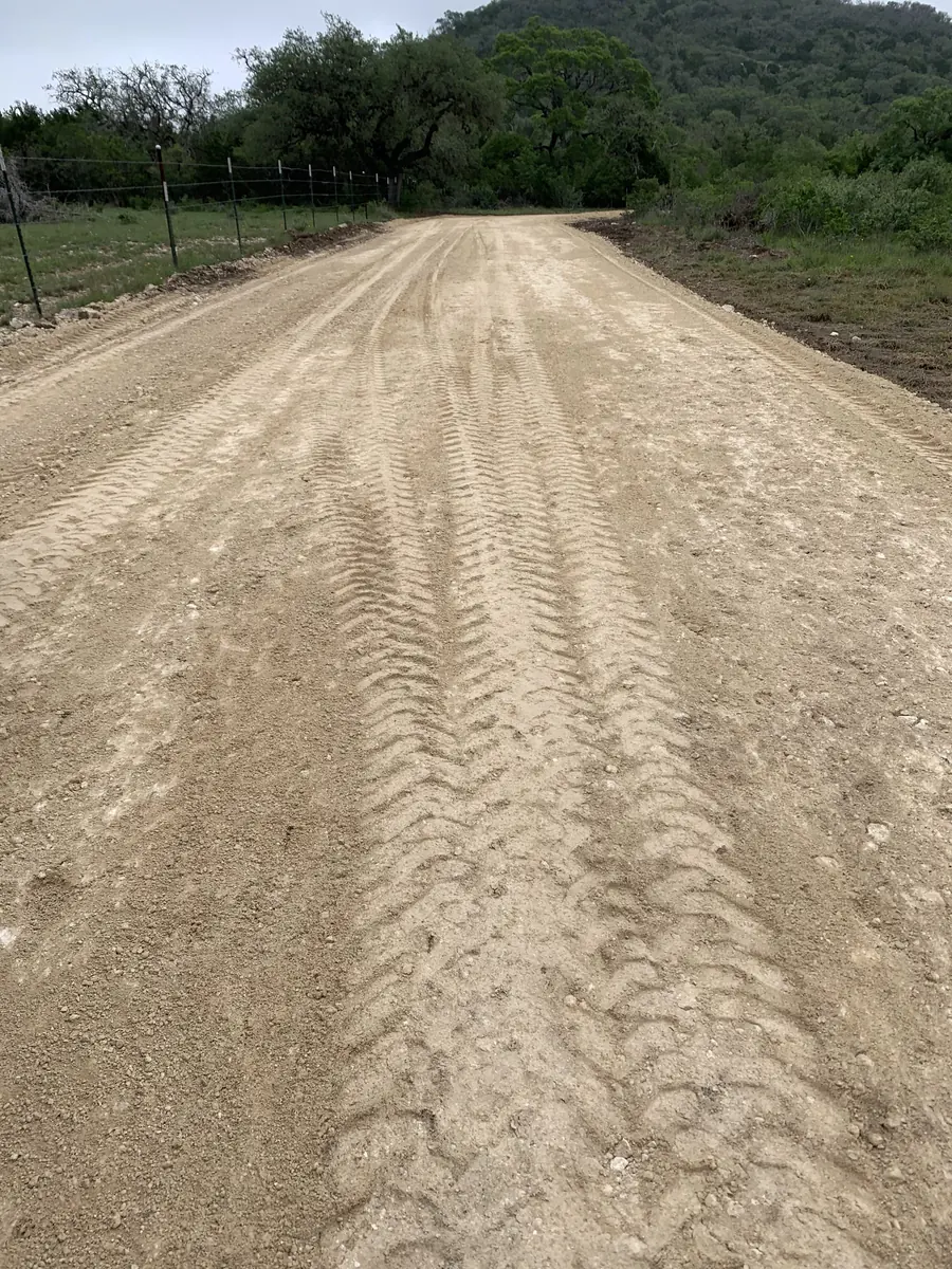 Wide graded road with tread marks, heading toward a wooded hill