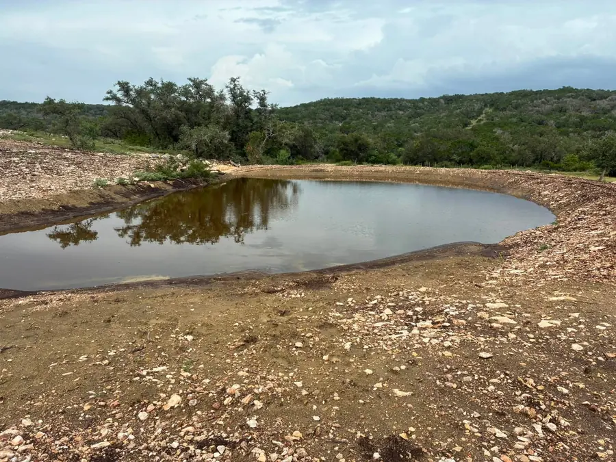 Newly dug stock pond holding water below wooded hills